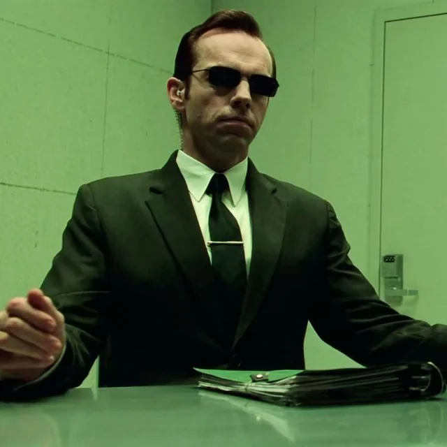 Character from the Matrix, Agent Smith, wearing a suit and sunglasses, looking serious and menacing